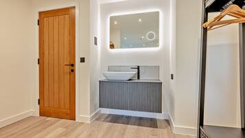 A modern bathroom with a wooden door, a vessel sink, and a mirror with integrated lighting.