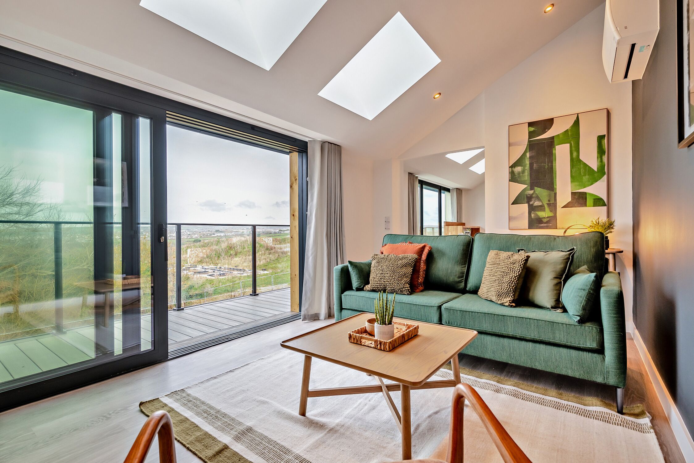 A spacious living room with a green sofa, a wooden coffee table, and a large window offering a view of the outdoors.