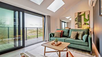 A spacious living room with a green sofa, a wooden coffee table, and a large window offering a view of the outdoors.