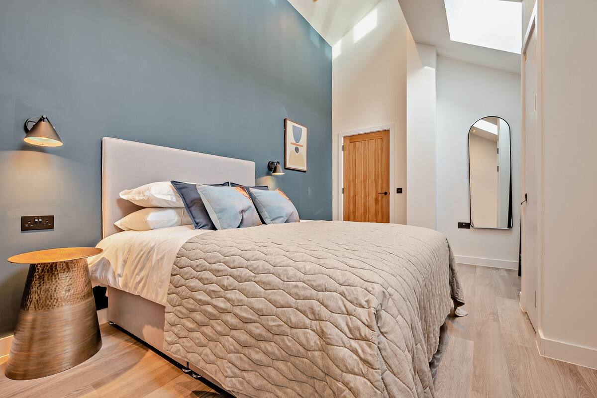A modern bedroom with a large bed, a bedside lamp, and a unique round side table.