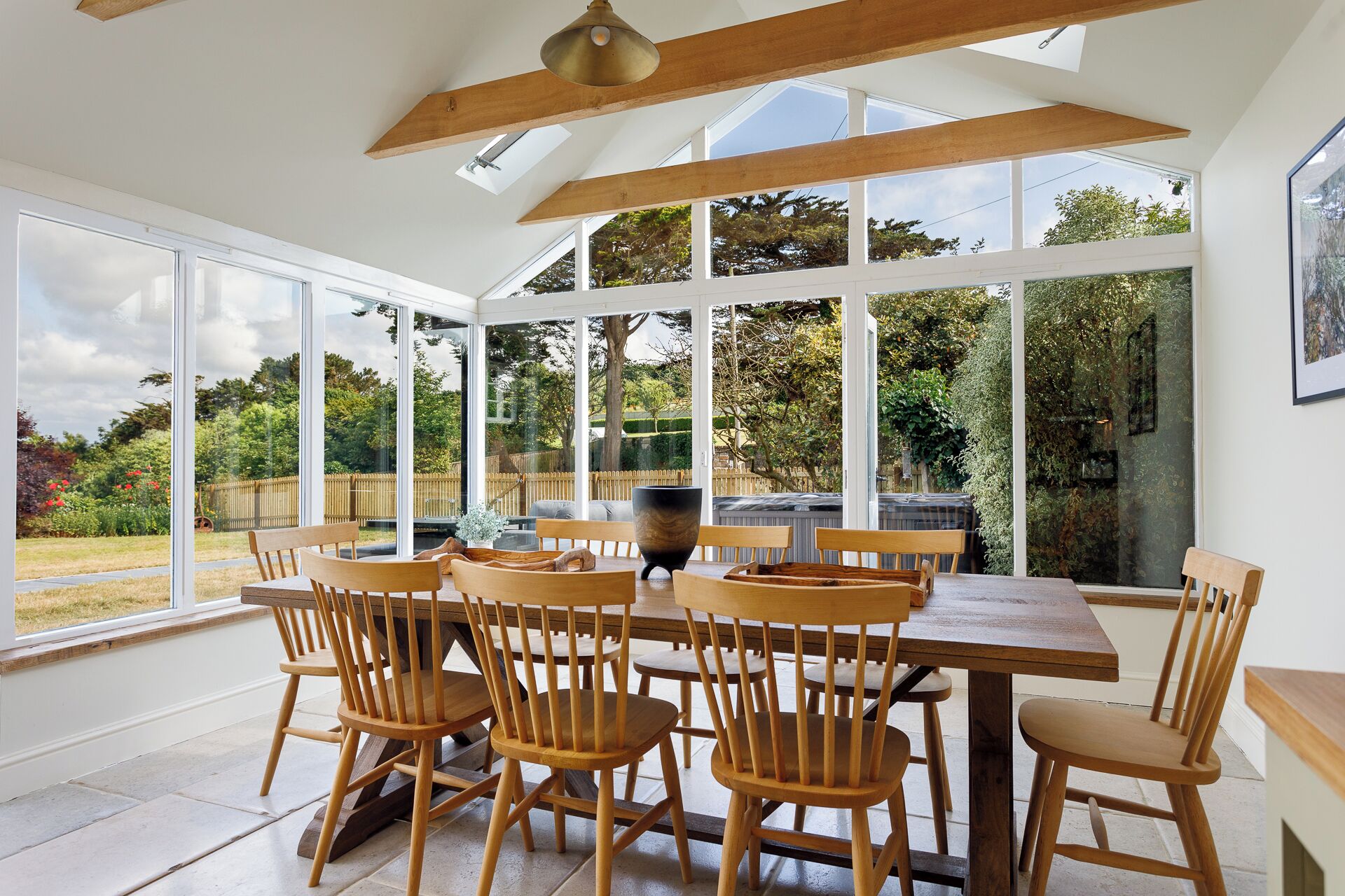 A conservatory with a wooden table and chairs, large windows, and a view of the garden.