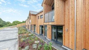 A row of modern wooden buildings with large windows and a landscaped garden area. - Landal Whalesborough (Bude)