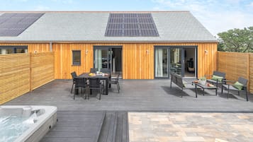 Ein Gebäude aus Holz mit einem geneigten Dach, Solaranlagen und einer Terrasse mit Gartenmöbeln.