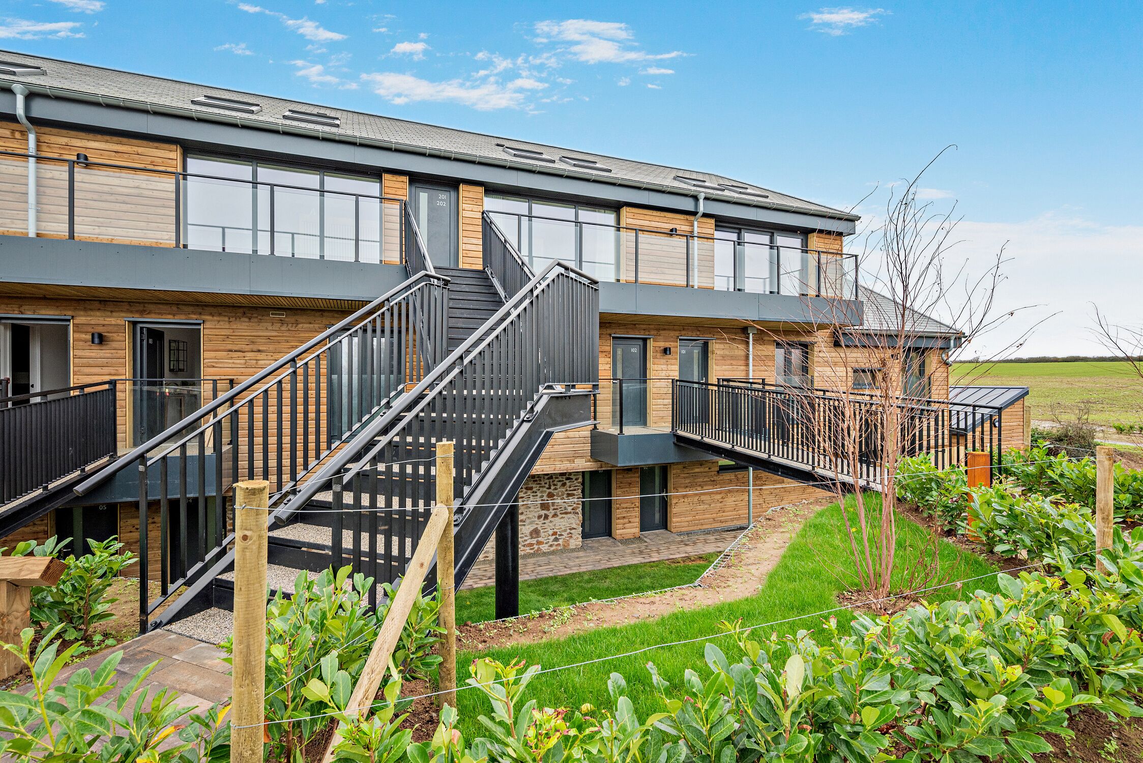 A modern building with a staircase leading to a balcony, surrounded by a well-maintained garden.