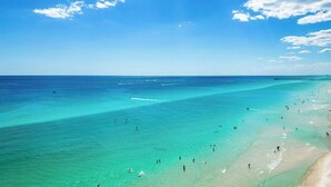 A beach with clear turquoise waters, a pier extending into the sea, and people enjoying the beach. - Beachfront Condo w/ Free Beach Service Near Pier Park (Panama City Beach)