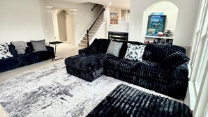 Ein modernes Wohnzimmer mit einer Eckcouch, einem schwarzen Hocker und einem gemusterten Teppich.