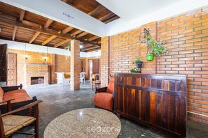 A spacious lobby with a brick wall, wooden ceiling beams, and a fireplace. There are seating areas with chairs and a sofa. - Large 3-bedroom House in Penha Sel0068 (Penha)