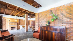 A spacious lobby with a brick wall, wooden ceiling beams, and a fireplace. There are seating areas with chairs and a sofa. - Large 3-bedroom House in Penha Sel0068 (Penha)