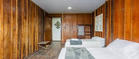 A wooden-finished room with two beds, a bench, and a door leading to another room.