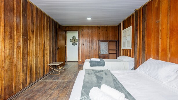 A wooden-finished room with two beds, a bench, and a door leading to another room. - Large 3-bedroom House in Penha Sel0068 (Penha)