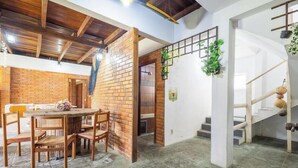 A dining area with a brick wall, wooden ceiling beams, and a staircase with a white railing. - Large 3-bedroom House in Penha Sel0068 (Penha)