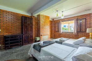 A room with brick walls, two beds, a wooden wardrobe, and a small table. - Large 3-bedroom House in Penha Sel0068 (Penha)