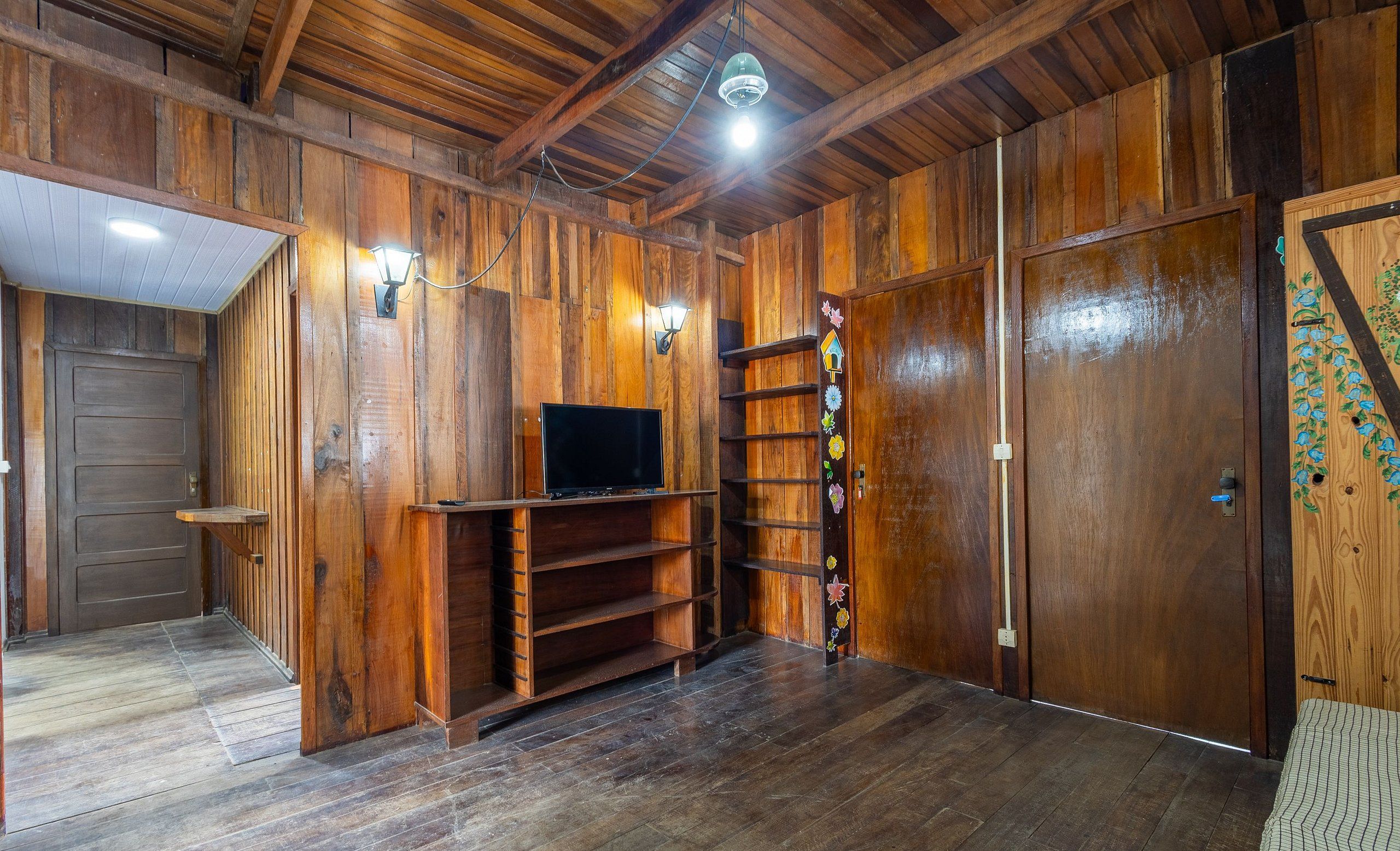 A wooden-paneled room with a TV on a shelf, a door with a decorative panel, and a light fixture on the ceiling.