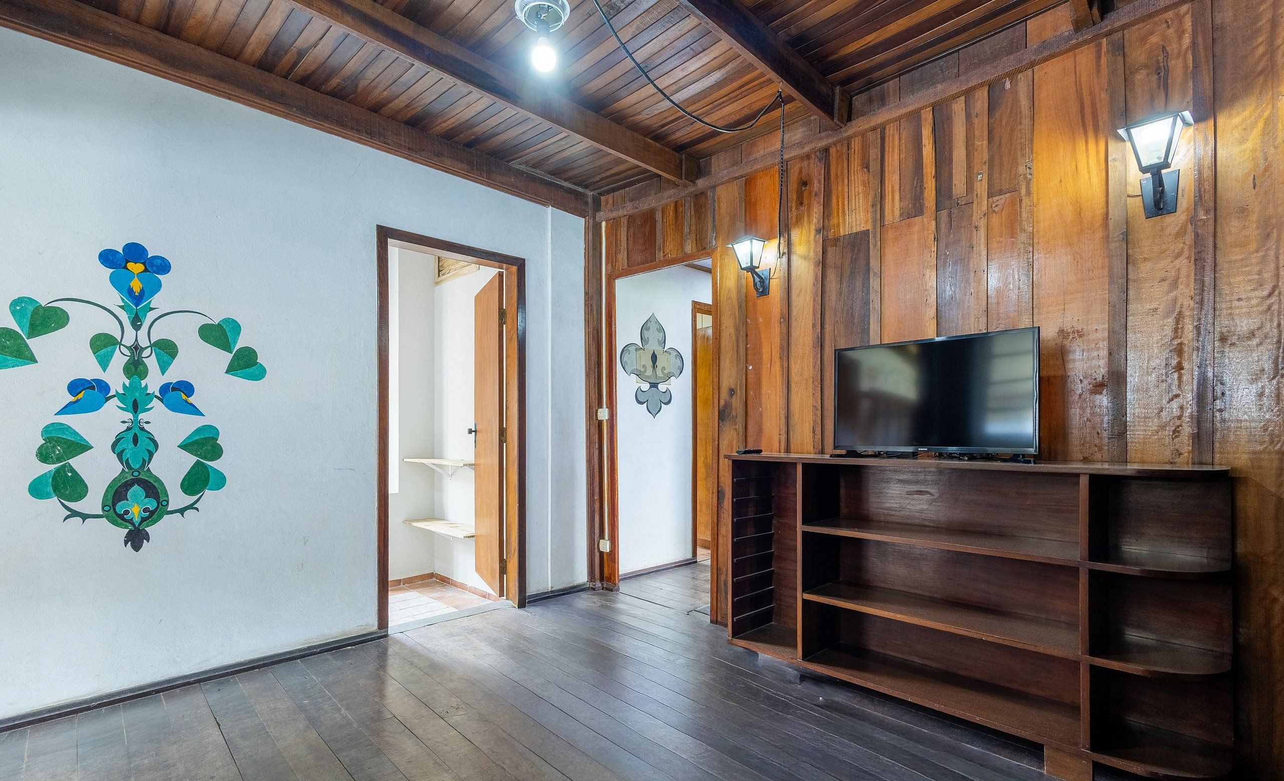 A spacious room with wooden walls and a dark wooden floor. There is a television on a wooden stand and a door leading to another room.
