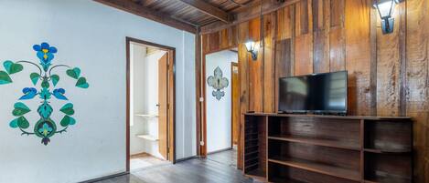 A spacious room with wooden walls and a dark wooden floor. There is a television on a wooden stand and a door leading to another room.