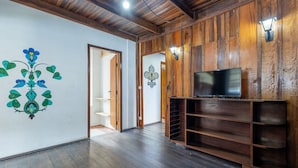 A spacious room with wooden walls and a dark wooden floor. There is a television on a wooden stand and a door leading to another room. - Large 3-bedroom House in Penha Sel0068 (Penha)