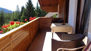 A balcony with a table and chairs, wooden railings, and a view of trees and mountains. - Our small vacation paradise with only 2 apartments is located in the middle of the mountains (Karersee)