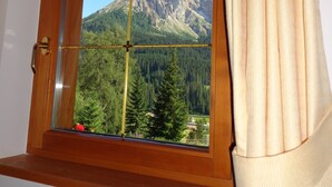 A window with a wooden frame and a view of a mountainous landscape. - Our small vacation paradise with only 2 apartments is located in the middle of the mountains (Karersee)