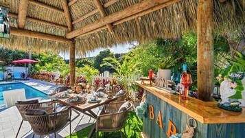 An outdoor bar area with a pool, wicker chairs, and a thatched roof.