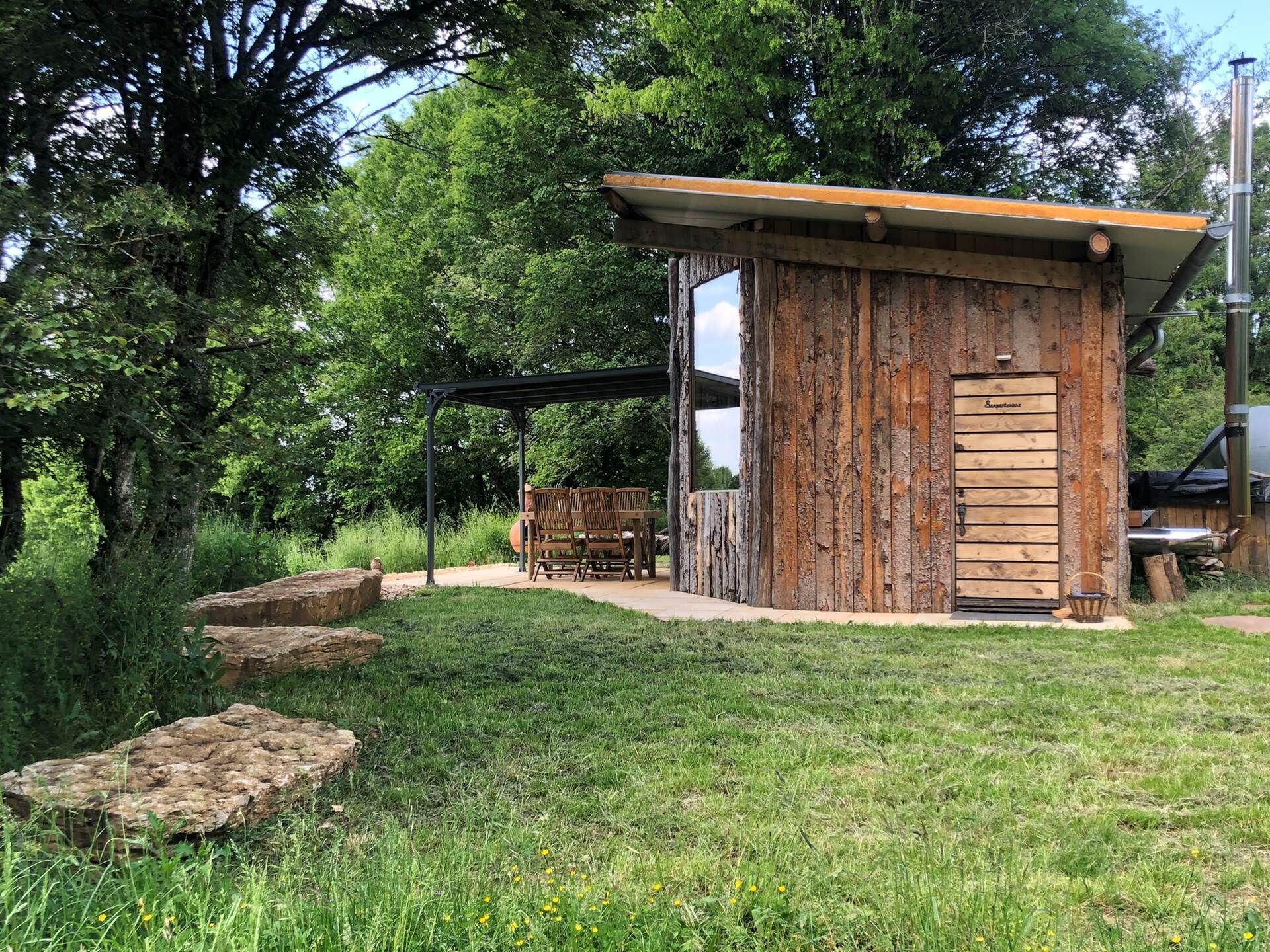 A rustic wooden cabin with a door labeled "Sonnenhaus" and a small outdoor seating area with chairs.