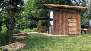 A rustic wooden cabin with a door labeled "Sonnenhaus" and a small outdoor seating area with chairs.