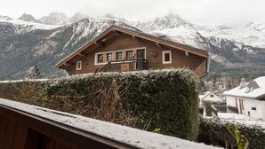 Una cabaña de madera con balcón, con montañas nevadas al fondo.
