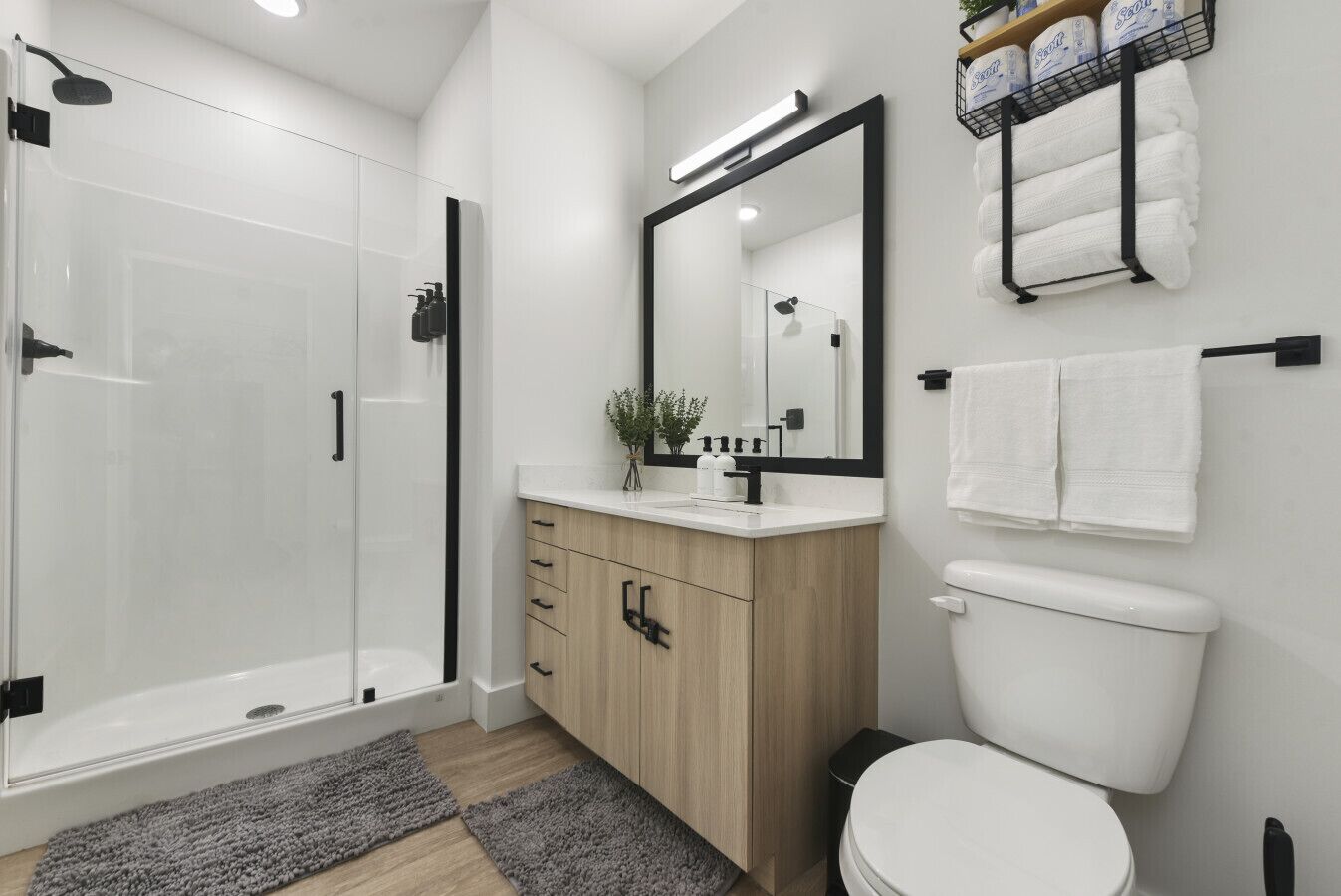 A modern bathroom with a glass shower enclosure, a wooden vanity, a white toilet, and a mirror above the sink.
