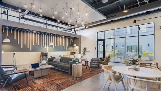 Un interior moderno con sofá, mesa de centro y comedor, que cuenta con un ventanal grande y un diseño de techo industrial.