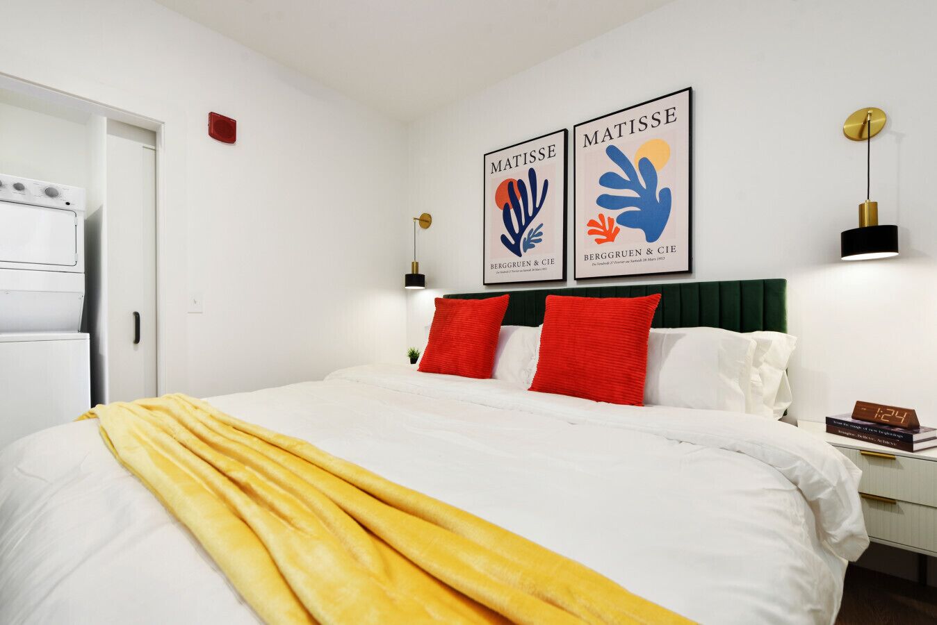 Una habitación de hotel con una cama, una mesita de noche, un reloj de pared y dos cuadros enmarcados sobre la cama.