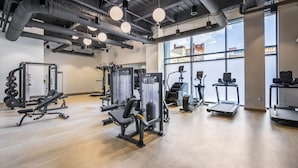 Ett modernt gym med olika typer av träningsutrustning, stora fönster och ett högt tak med synliga ventilationskanaler.