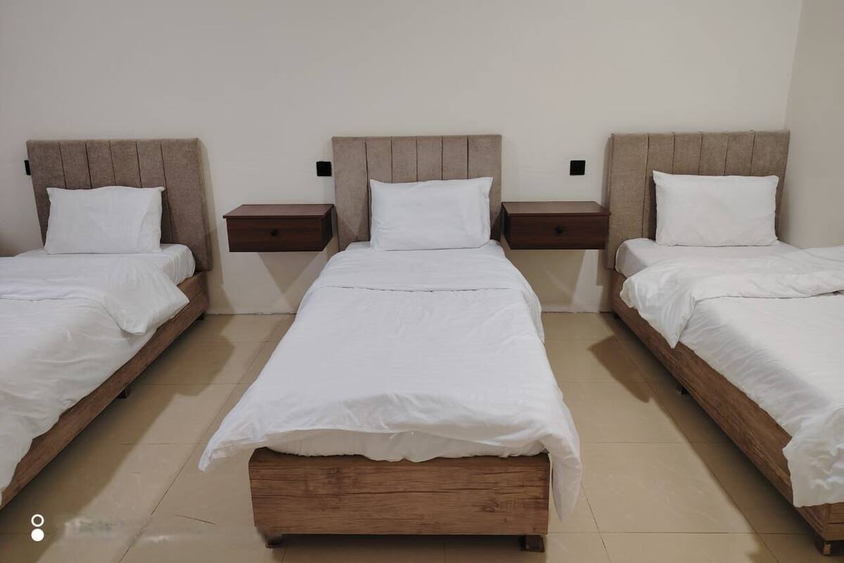 A hotel room with three single beds, each with a wooden headboard and white bedding.