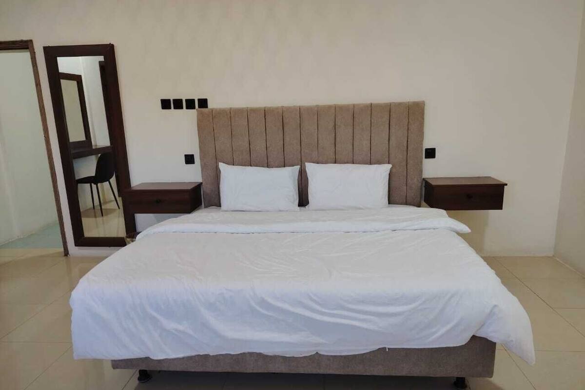 A bedroom with a bed, nightstands, a mirror, and a chair.
