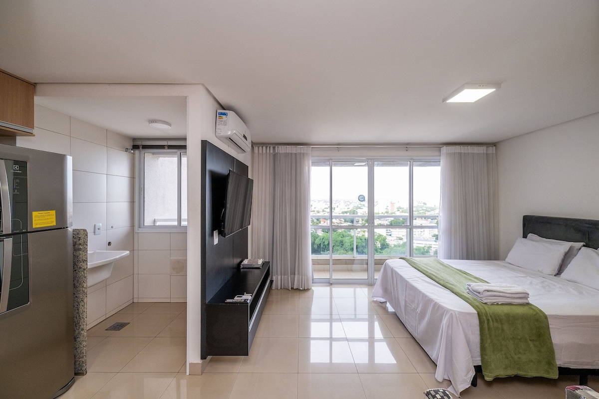 A hotel room with a bed, a TV, a sink, and a window with a view.