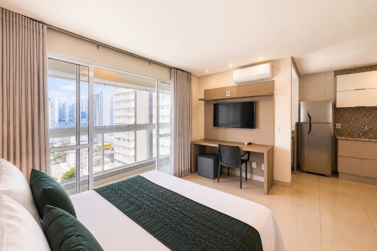 A hotel room with a bed, a desk, a TV, and a kitchenette.