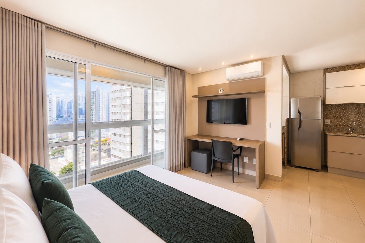 A hotel room with a bed, a desk, a TV, and a kitchenette.