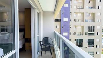 A balcony with a bed, a chair, and a view of a multi-story building.