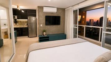 Una habitación de hotel moderna con cama, televisor, kitchenette y vistas a la ciudad.