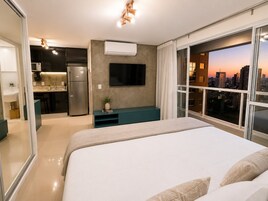 Una habitación de hotel moderna con cama, televisor, kitchenette y vistas a la ciudad.