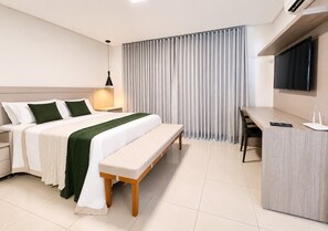 A modern hotel room with a bed, bedside table, bench, desk, and a TV. - The Expression (Goiânia)