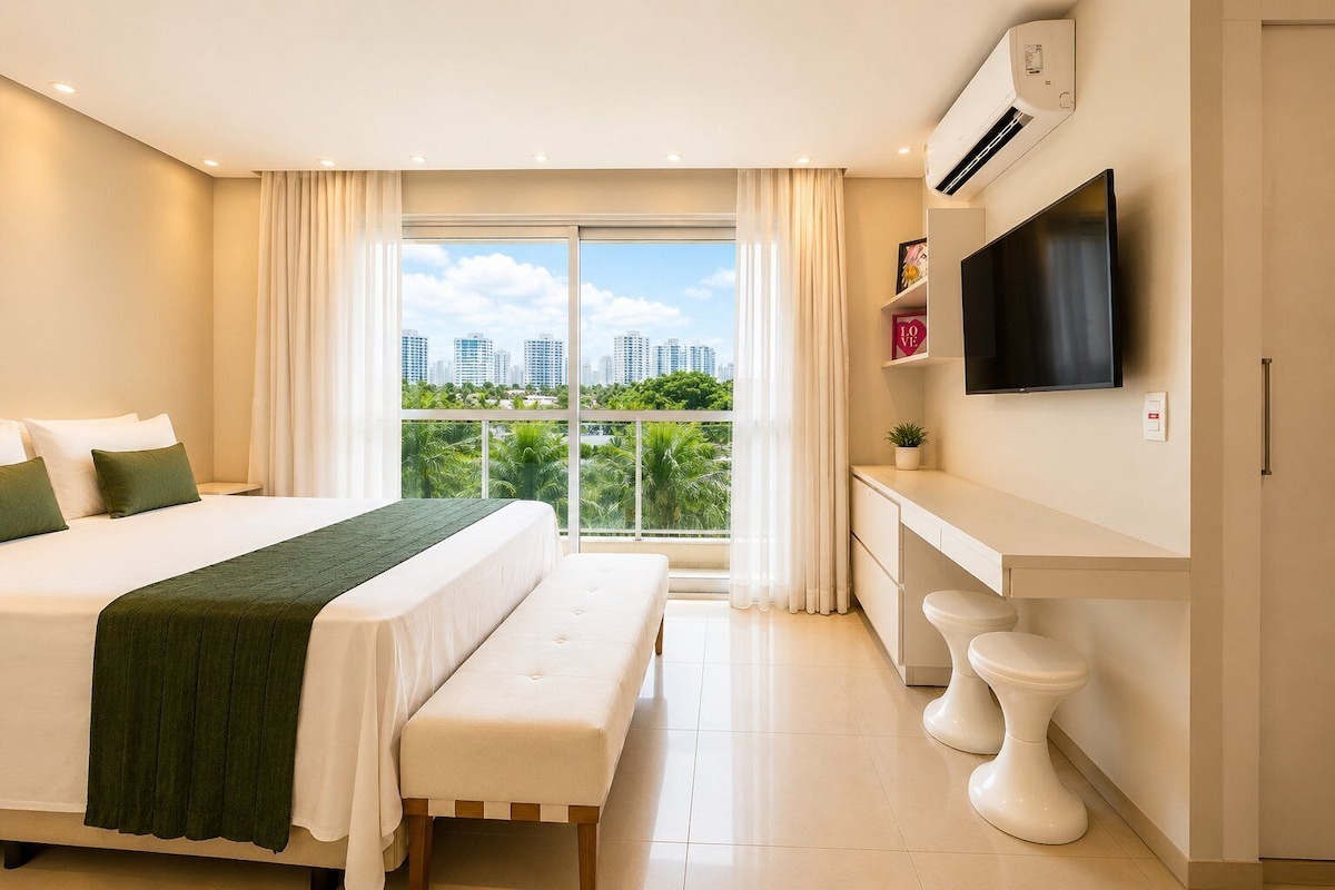 A modern hotel room with a large bed, a bench, a TV, a small desk, and a toilet.