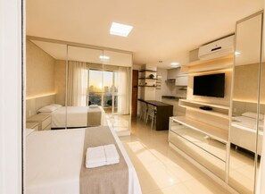 A modern hotel room with a bed, a desk, a television, and a kitchen area. - The Expression (Goiânia)