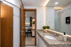 A modern bathroom with a wooden door, a sink, a mirror, and a shower area. - The Expression (Goiânia)