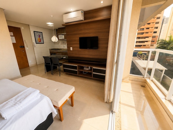 A modern hotel room with a bed, a TV, a dining area, and a balcony with a view of the city. - The Expression (Goiânia)