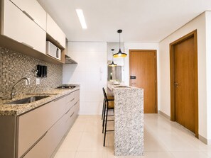 A modern kitchen with a marble countertop, stainless steel sink, and a wooden door. - The Expression (Goiânia)