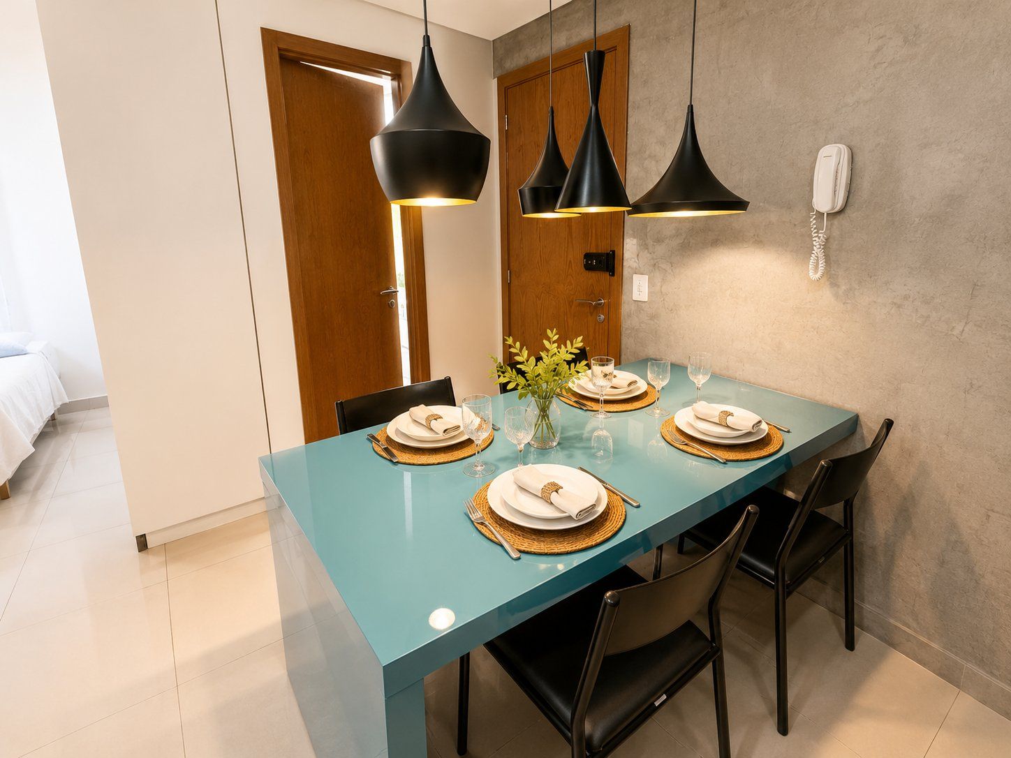 A dining area with a teal table, black chairs, and pendant lights.