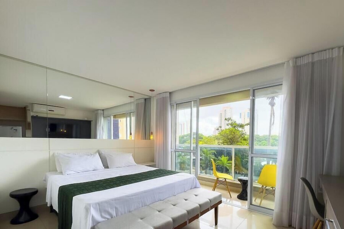 A modern hotel room with a large bed, a balcony with a view, and a separate seating area.