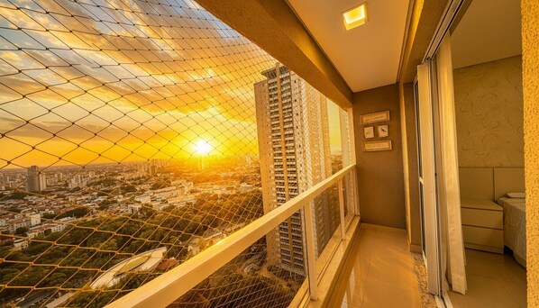 A balcony with a view of a cityscape during sunset, a window with a view of tall buildings, and a door leading to a room. - The Expression (Goiânia)