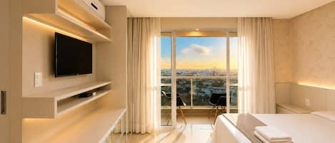 A hotel room with a bed, a TV, a desk, and a large window with a city view.
