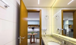 A modern bathroom with a large mirror, a sink, and a hairdryer mounted on the wall. - The Expression (Goiânia)