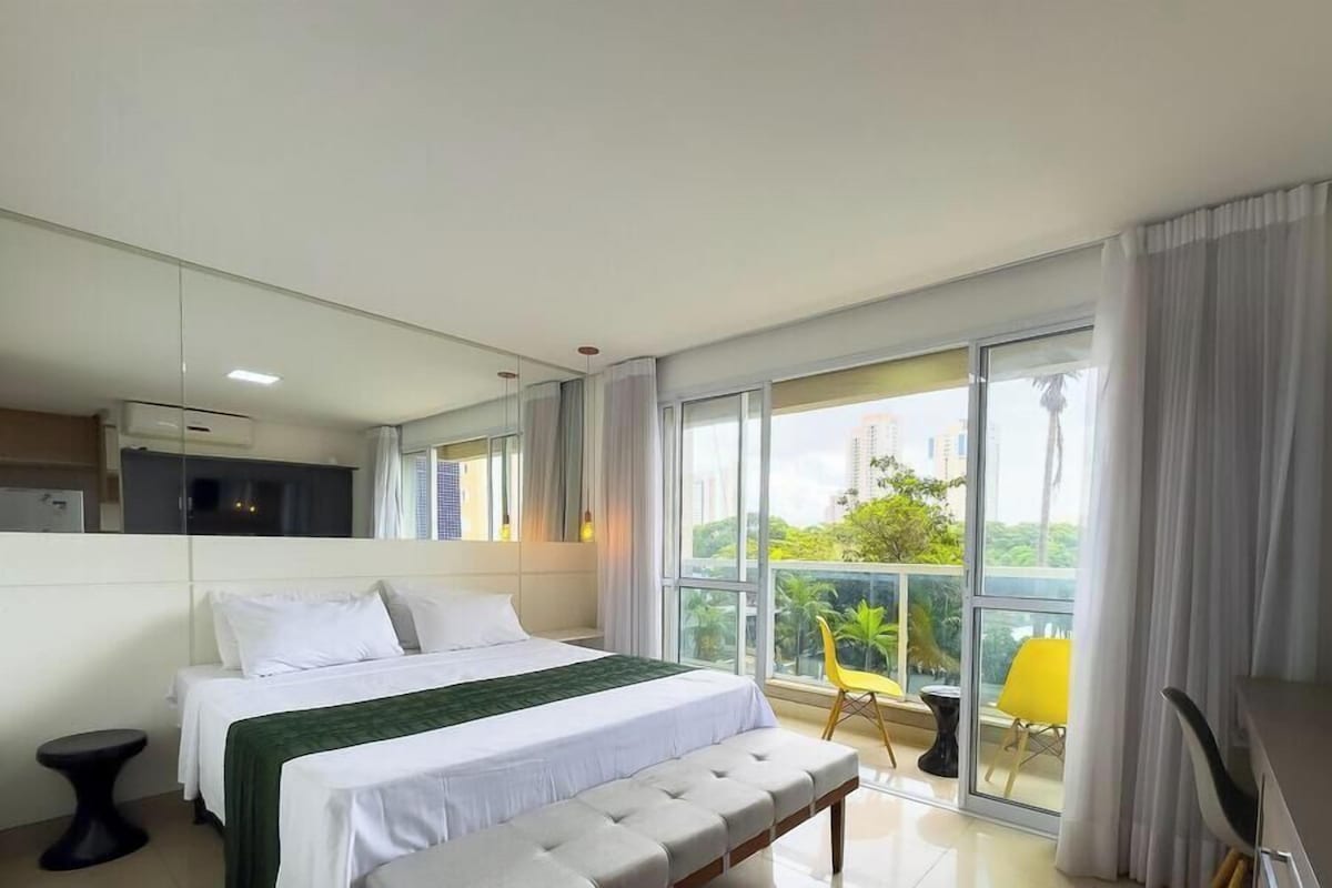 A modern hotel room with a large bed, a balcony with a view, and a separate seating area.